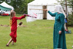 A youth rides a hobby horse and "spears" a water balloon hanging from a pole.